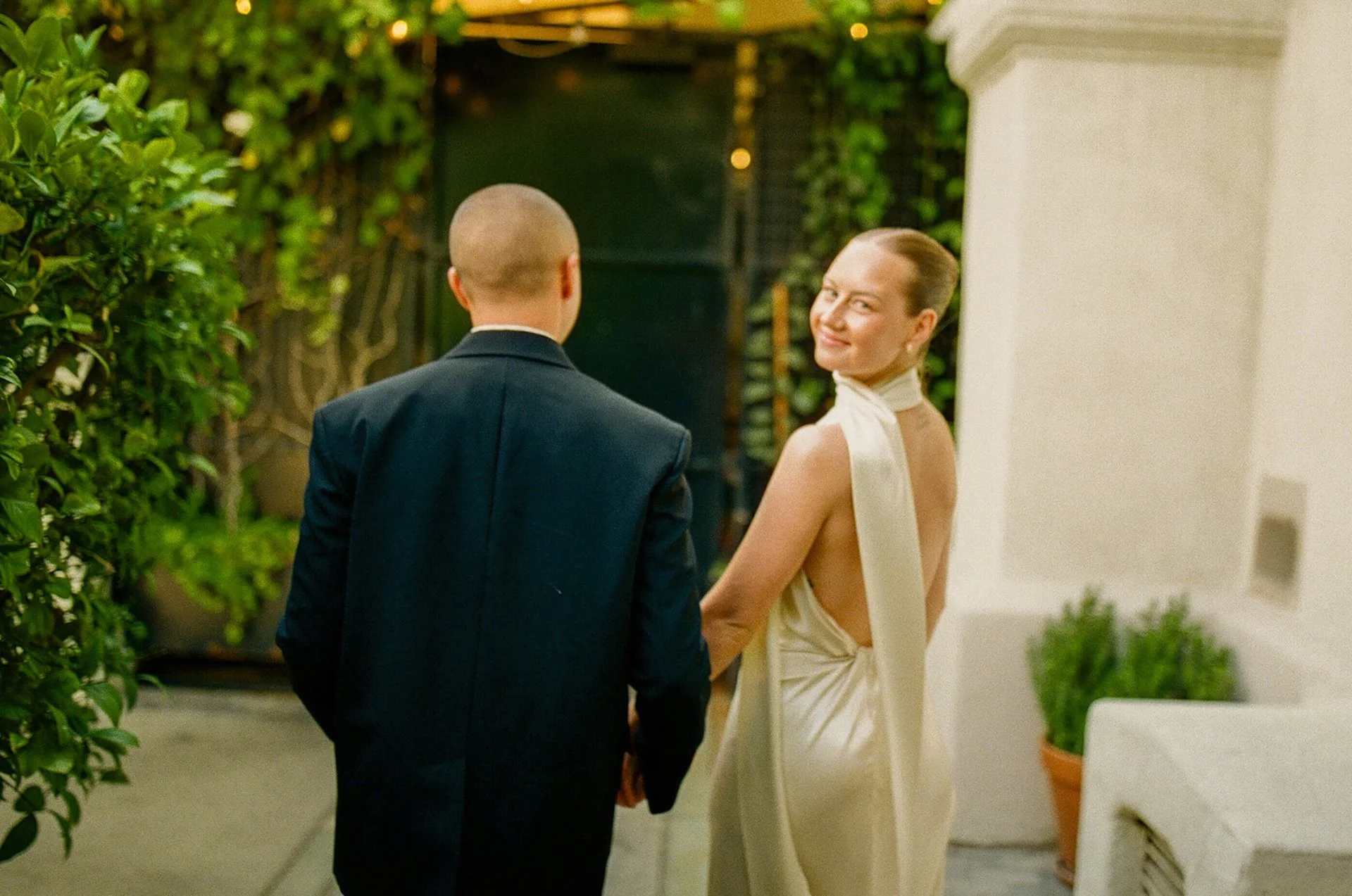 The couple walking hand in hand toward the reception area, with greenery and string lights creating a romantic garden atmosphere for Intimate Wedding Ideas.