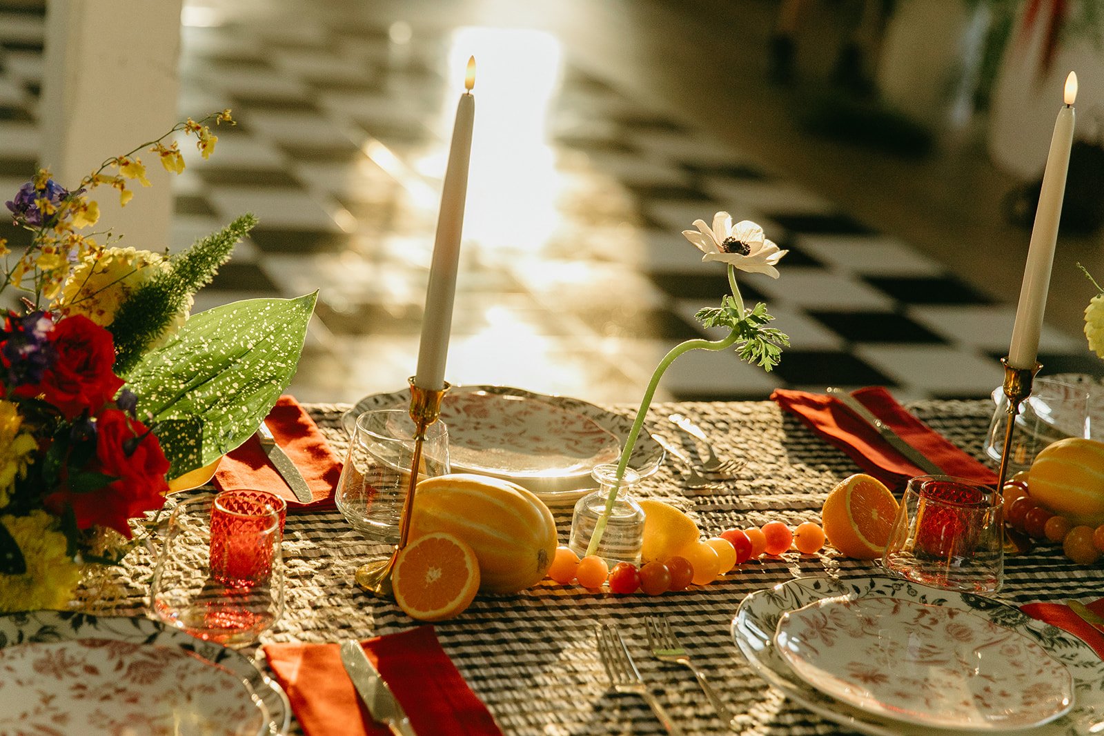 A styled reception table at The Revery LA with candles, citrus, florals, and patterned linens glowing in warm evening light.