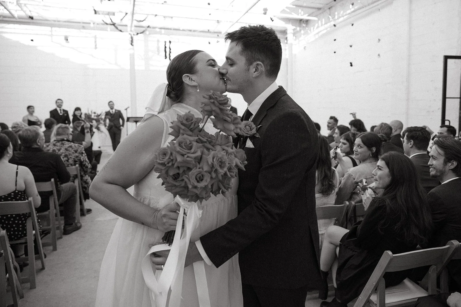 The couple sharing their first kiss after the ceremony at The Revery LA as guests look on from their seats.