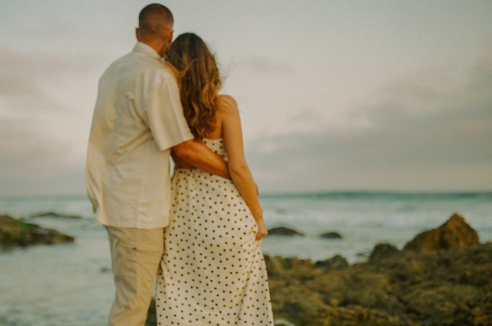 A couple looking out at the ocean in outfits that are perfect for what to wear for engagement photos