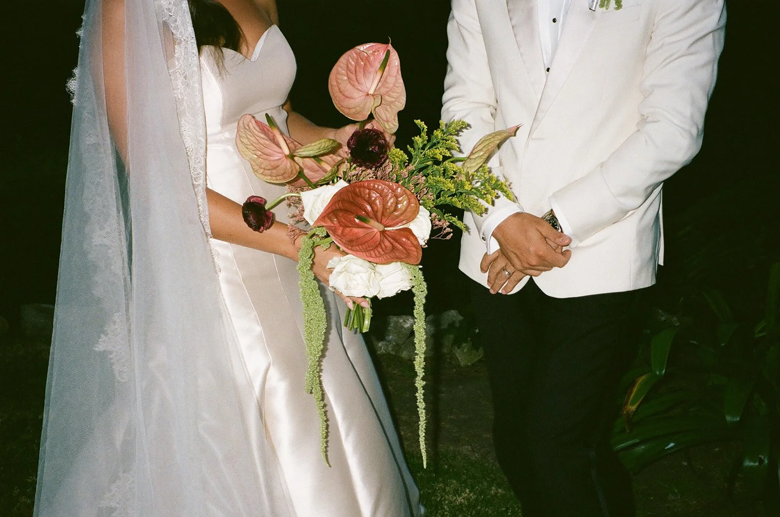 Close-up of the couple holding a modern bouquet with cascading greenery during nighttime portraits.