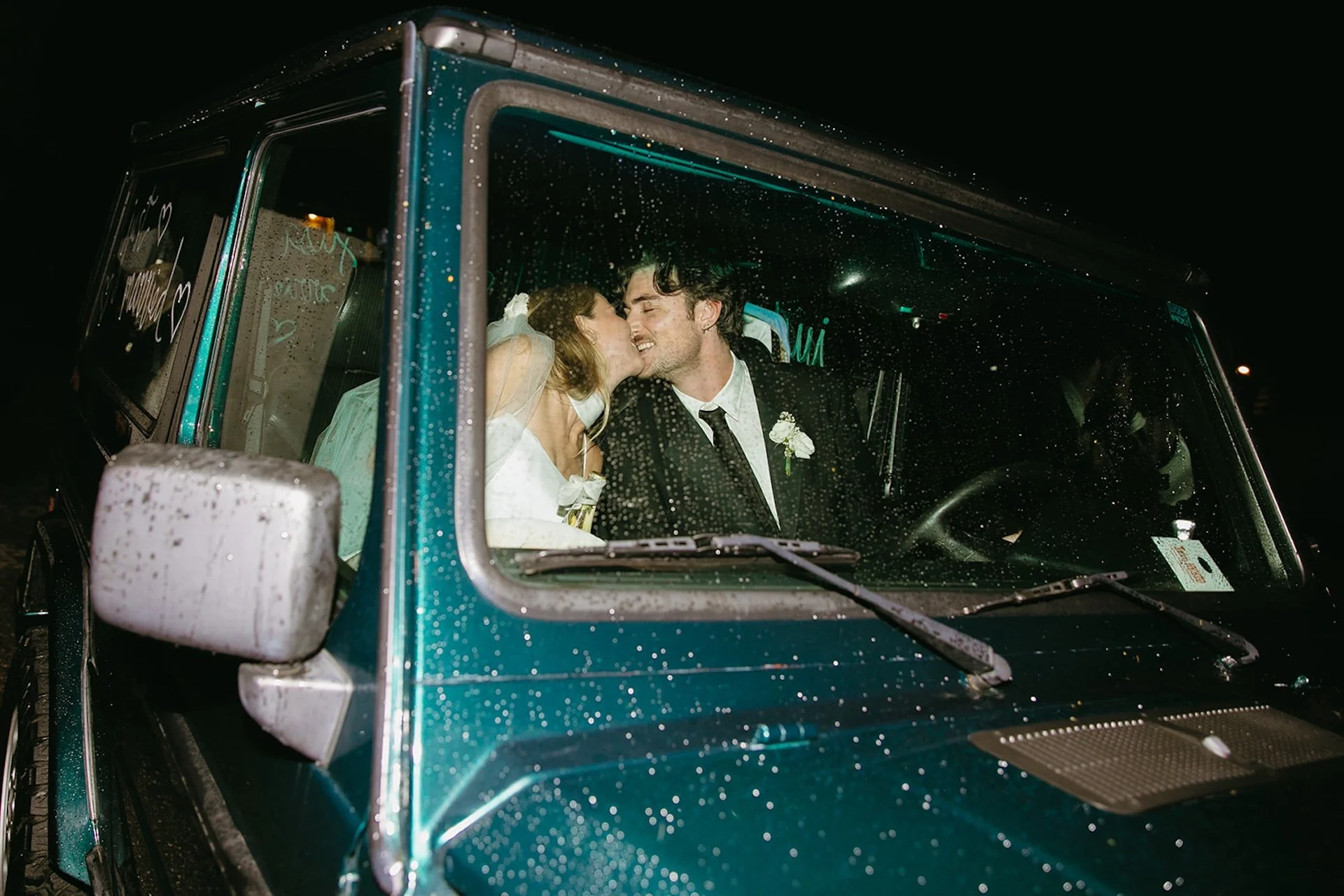 A flash photo of the bride and grom sharing a kiss in an old Jeep for their send off after their Laguna Beach wwedding.