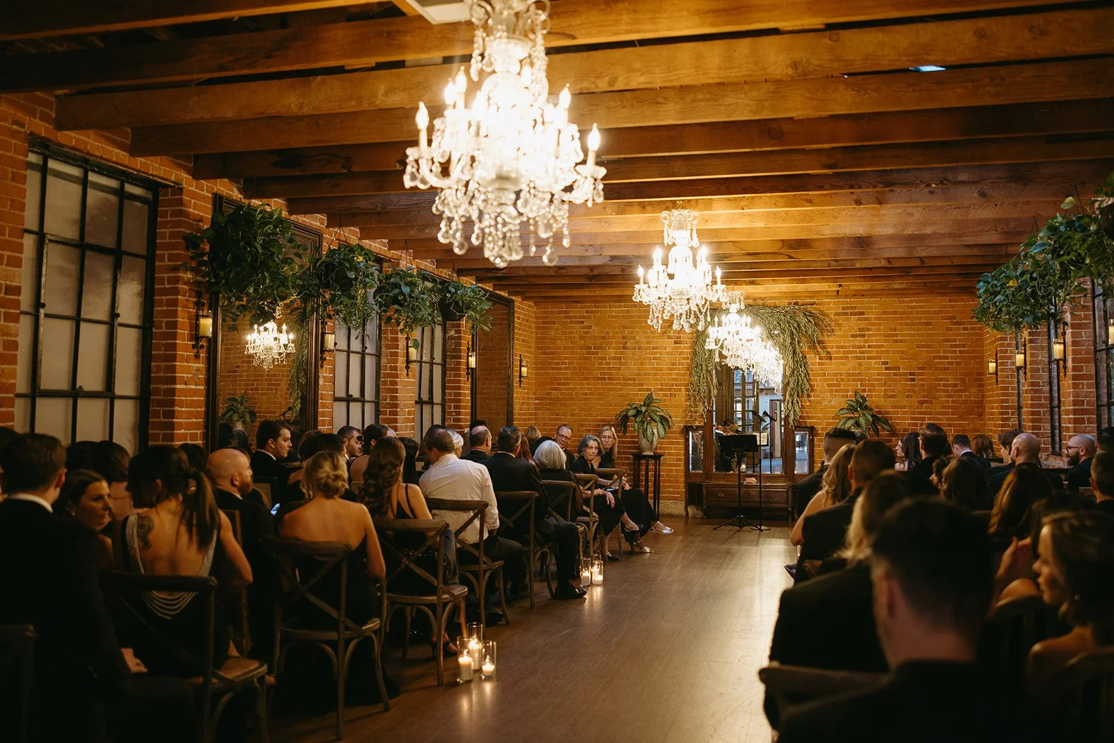 An indoor wedding ceremony held at one of the most elegant DTLA wedding venues, featuring exposed wood beams, brick walls, and grand crystal chandeliers.