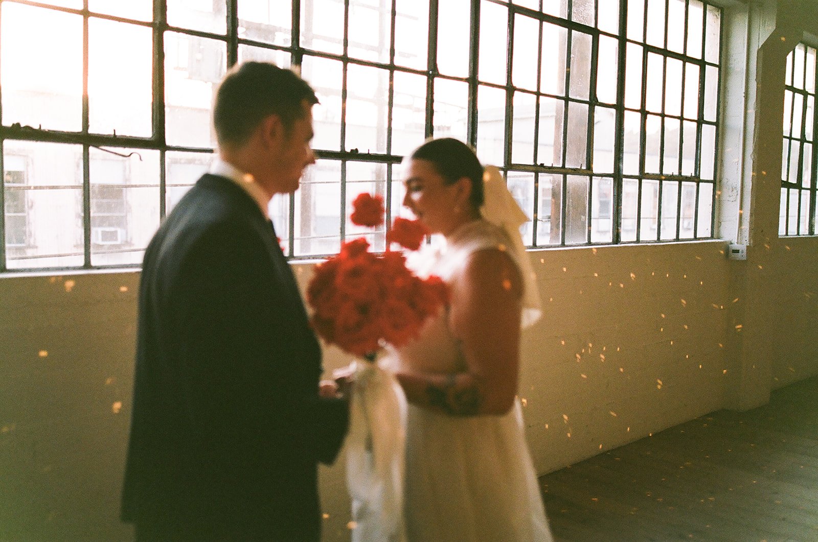A soft, slightly blurred portrait of the couple holding a bouquet together near the windows at The Revery LA with light bouncing around them.