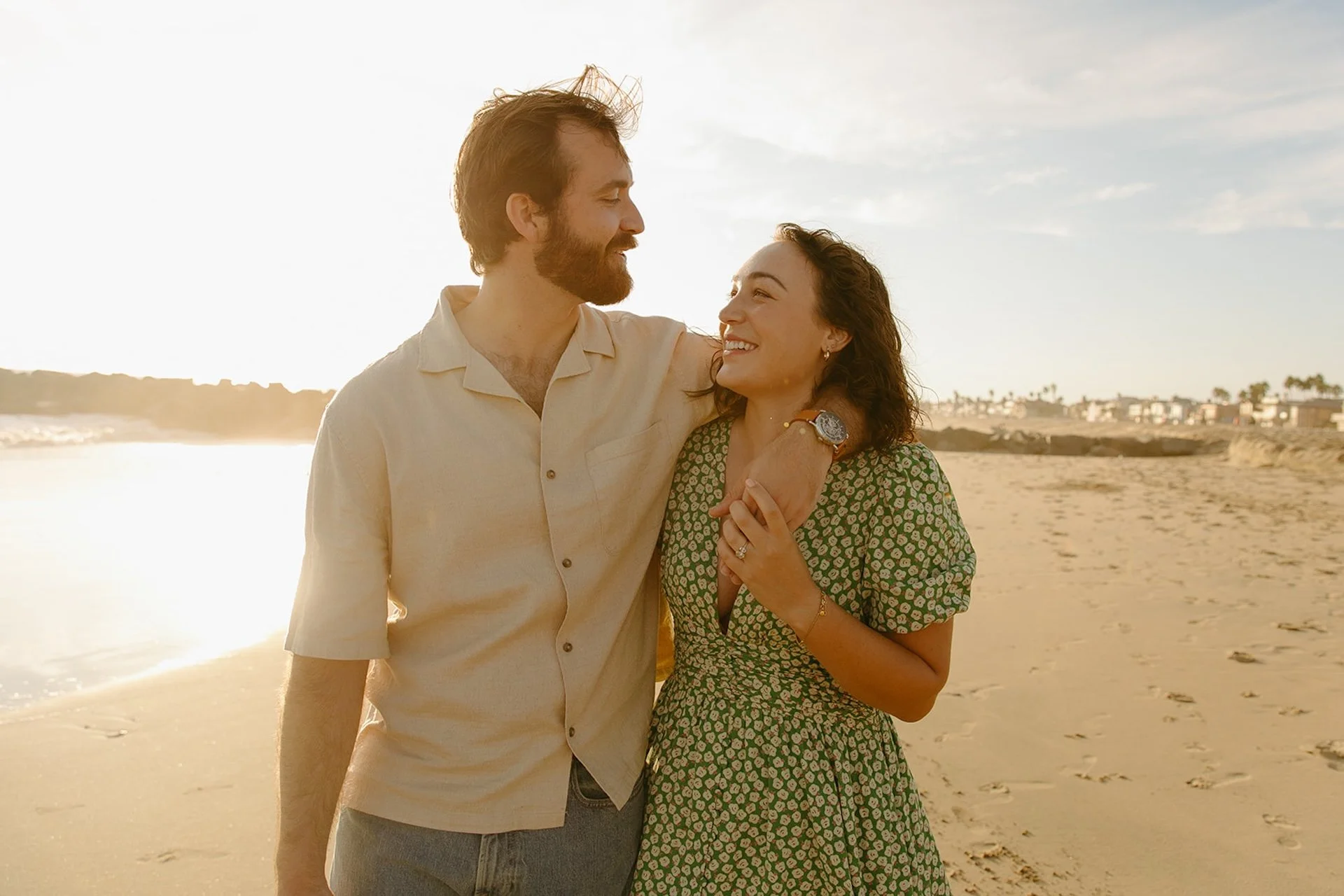 Smiling couple walking arm in arm along the shoreline during their newport beach engagement photos with soft golden hour light and ocean backdrop.