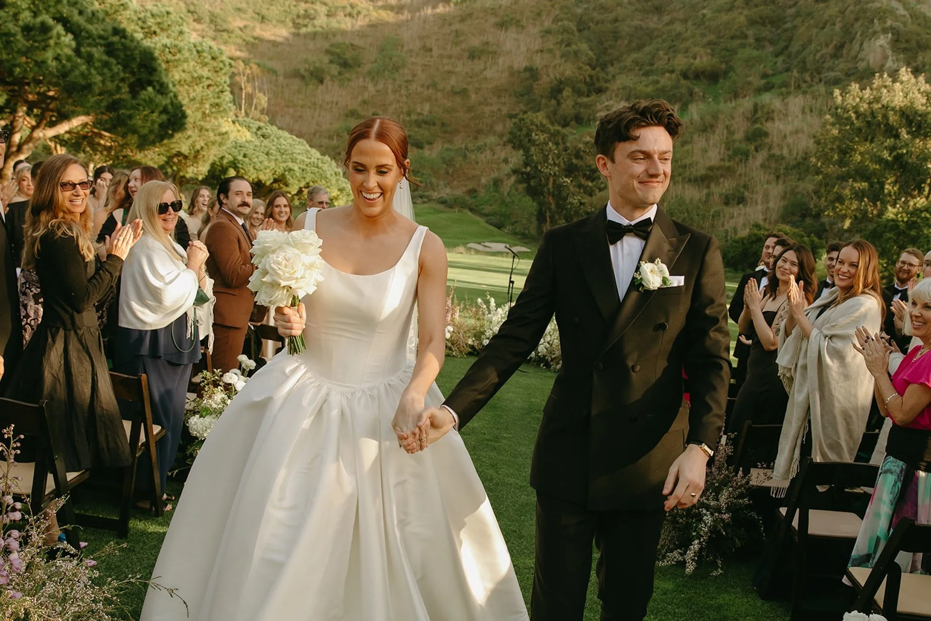 Newlyweds walking down the aisle after their ceremony as guests applaud on the canyon lawn.