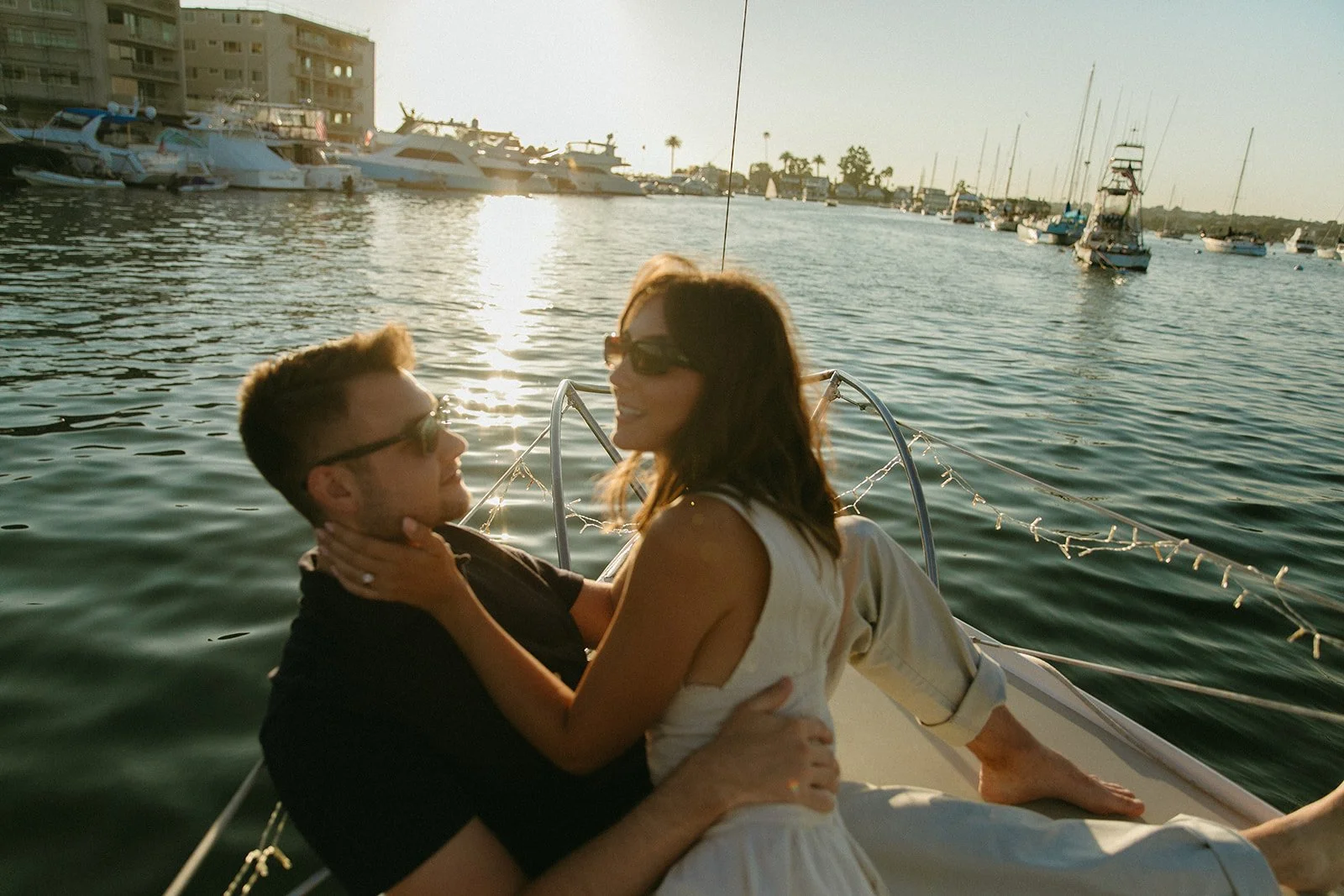 Couple lounging together on a sailboat at sunset, sunset sailboat engagement photos with calm harbor views.