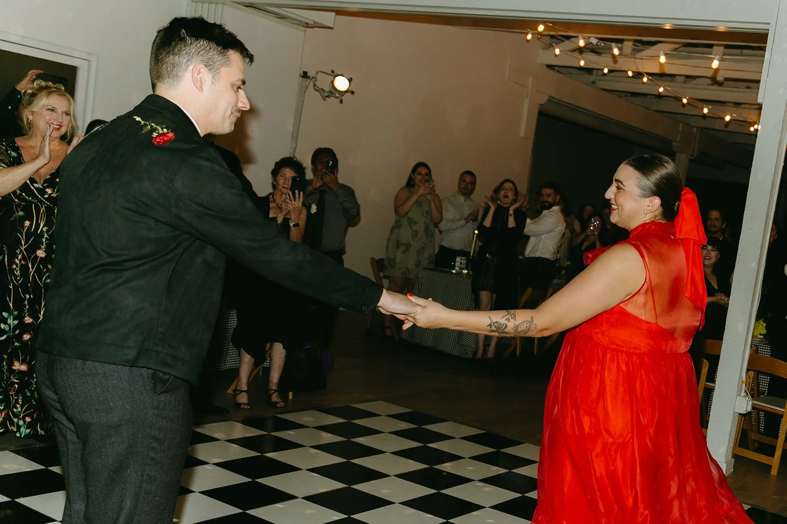 The couple holding hands and dancing together on the checkered dance floor at The Revery LA as guests cheer them on.