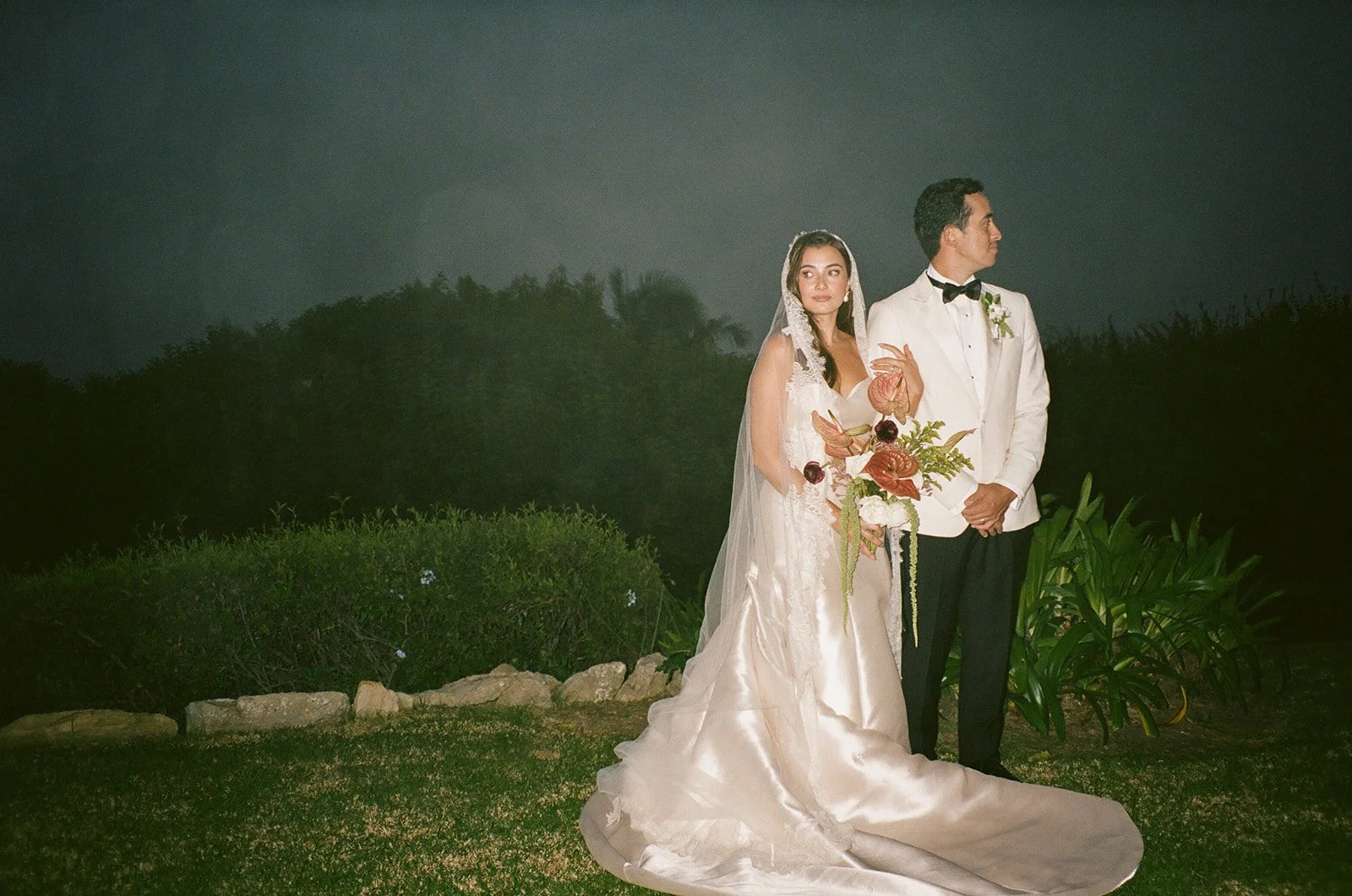 The couple standing side by side holding hands during nighttime portraits under a deep blue sky.