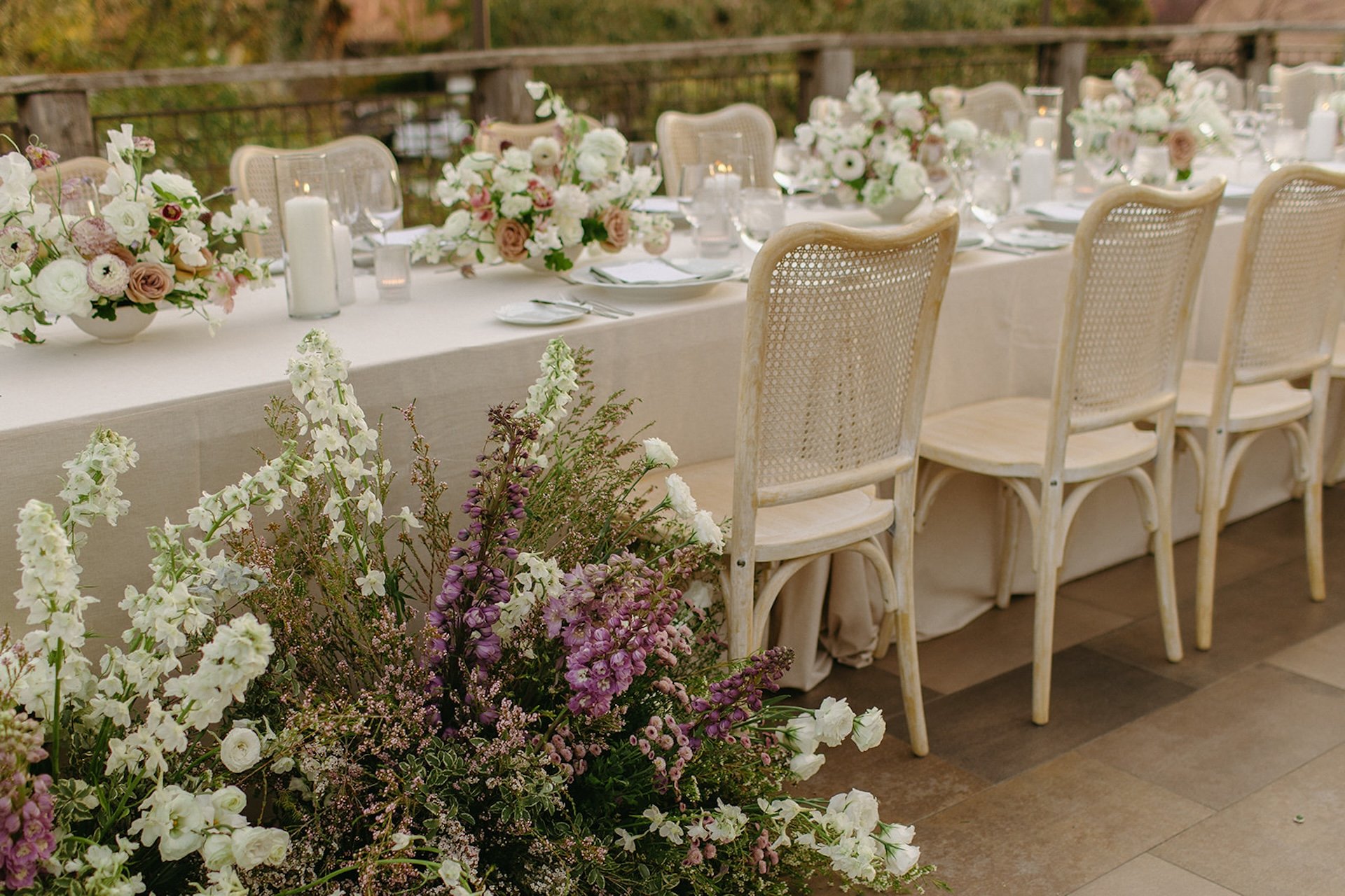 Close up of reception table florals in blush, ivory, and soft lavender tones styled along a long dinner table.