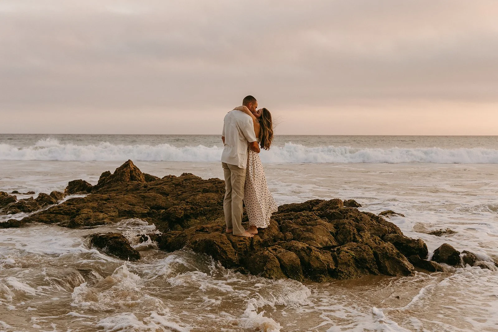 A couple kissing on ocean rocks and showing what to wear for engagement photos