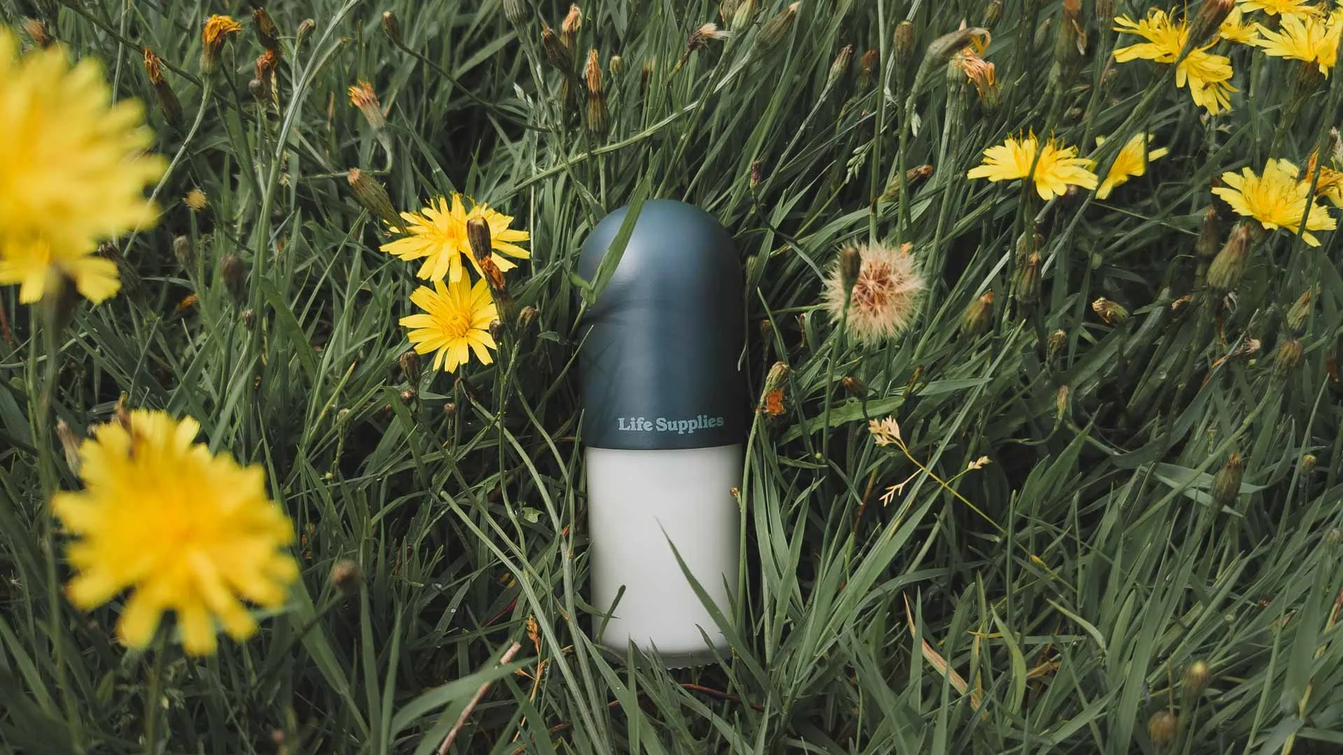 A Life Supplies roll-on antiperspirant bottle lying on grass surrounded with dandelions.