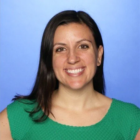A woman with long dark hair, smiling, wearing a green top, against a blue background.