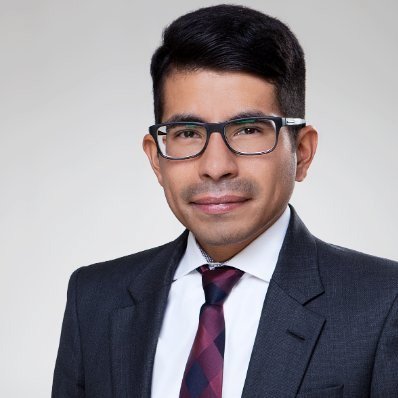 Professional man in business suit with glasses posing against a plain background.