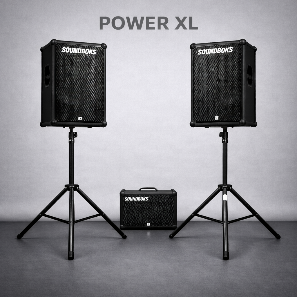 Zwei große schwarze Lautsprecher auf Stativen und ein kleines tragbares Lautsprechersystem vor einer grauen Wand, mit der Aufschrift "POWER XL" darüber.