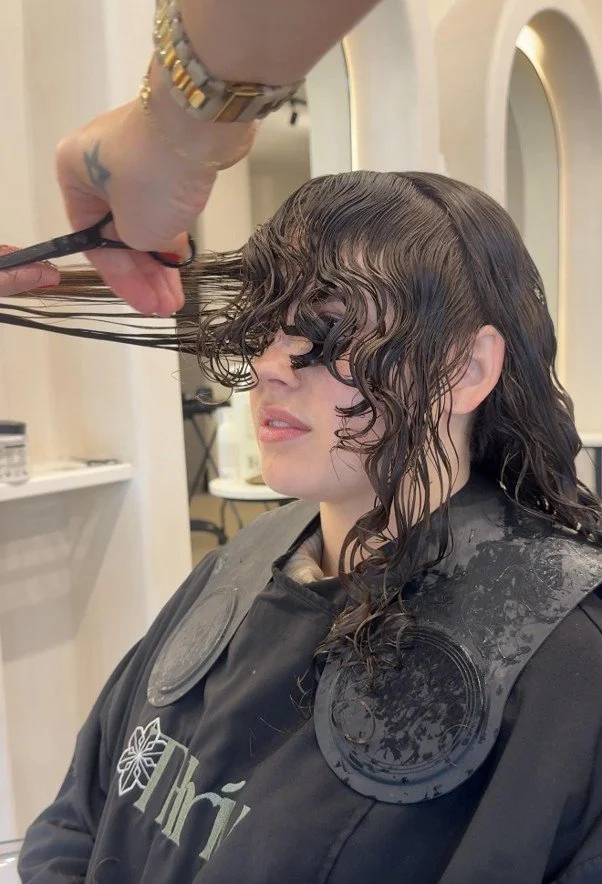 Stylist wet cutting the front sections of a client’s curly hair at Thriv