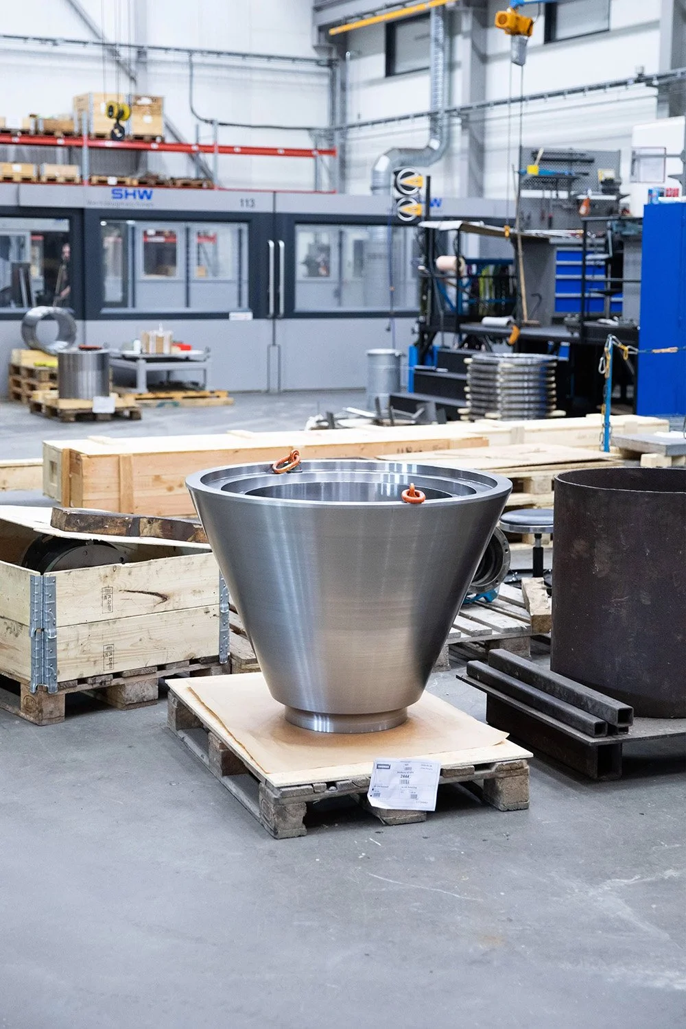 En konformad maskindel står på en lastpall i en verkstad.