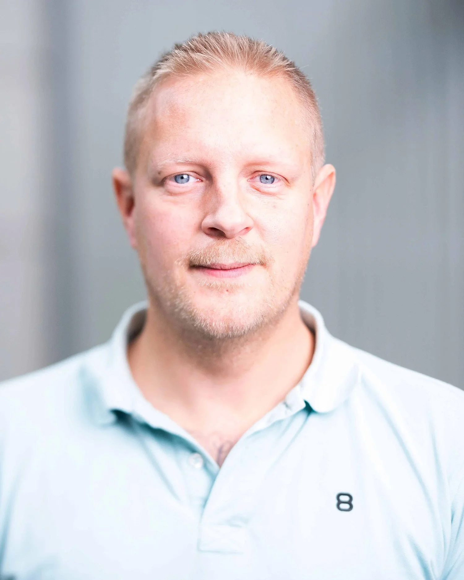 Porträttbild på man med ljust hår, blåa ögon och en ljusblå T-shirt, mot neutral bakgrund.