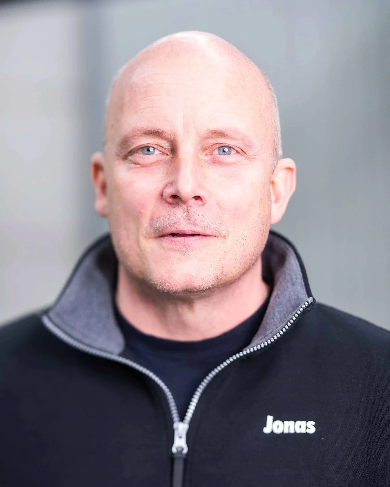 Porträtt av en skallig man med blå ögon, svart tröja, mot neutral bakgrund.