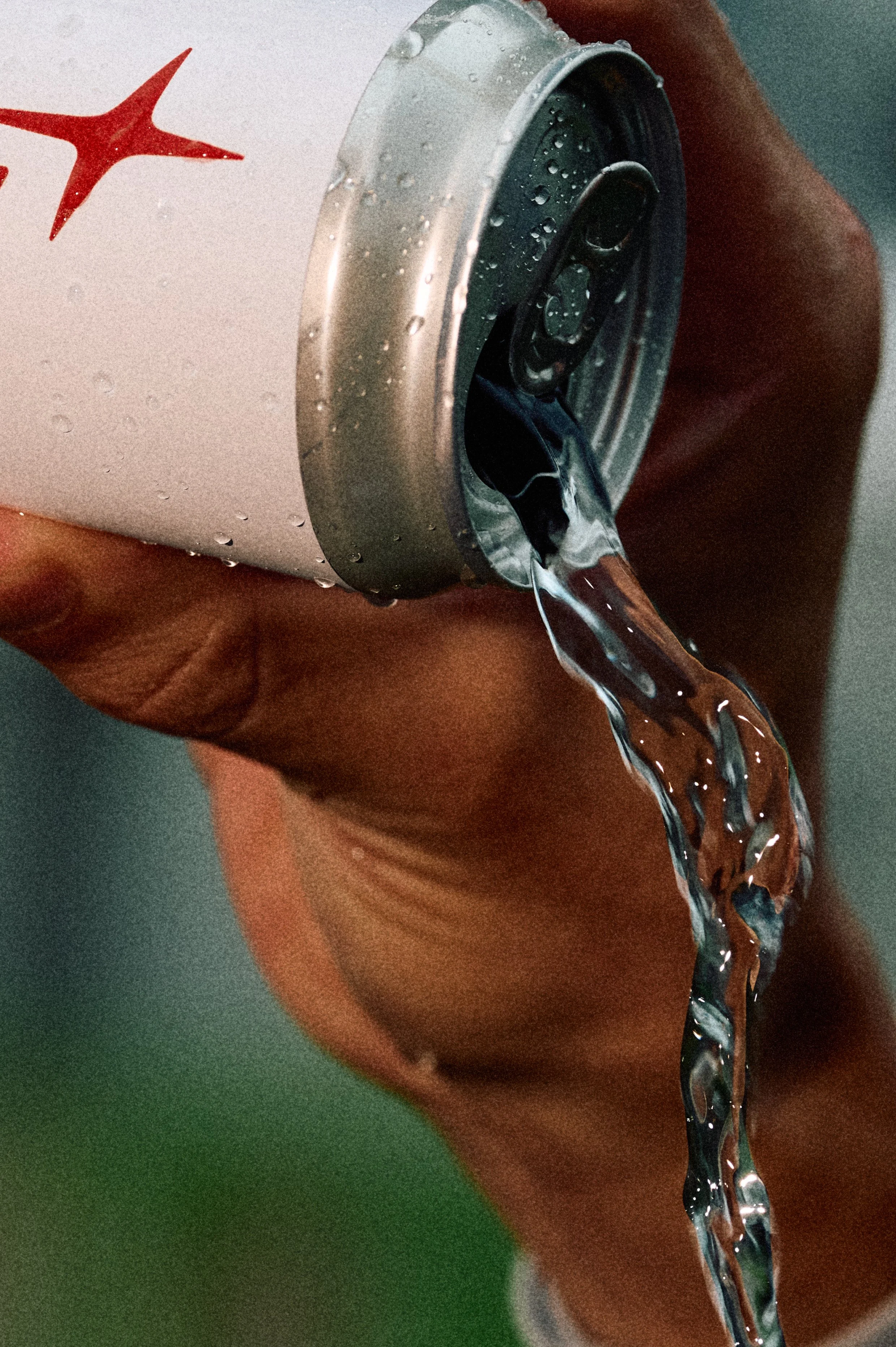 A person holding a can of a beverage, with liquid pouring out of the open tab.