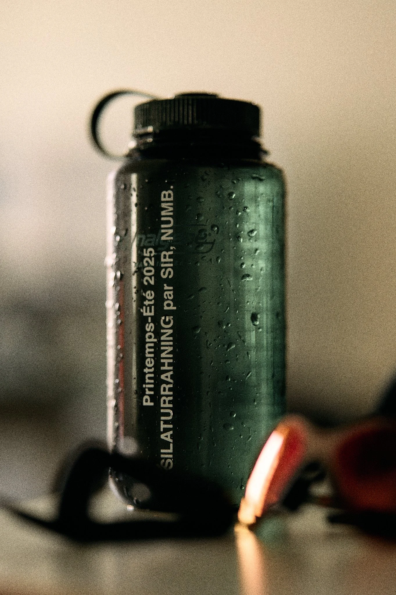 Close-up of a black water bottle with water droplets, showing a label with text.