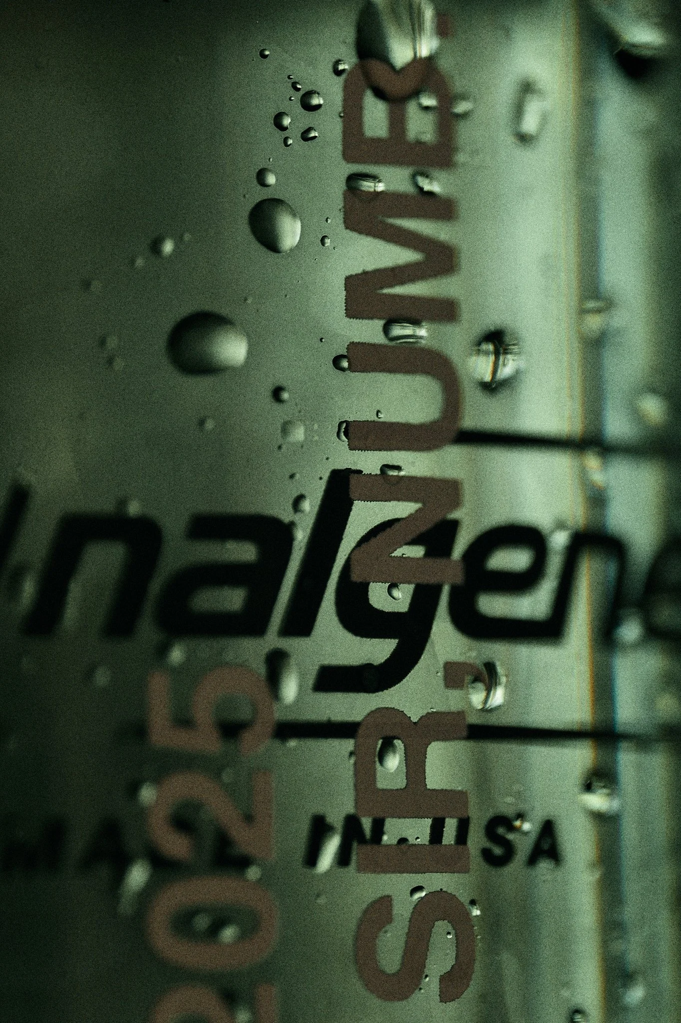 Close-up of a metallic surface with water droplets and partially visible text reading 'SLEVEL'. The surface appears to be a reflective material.