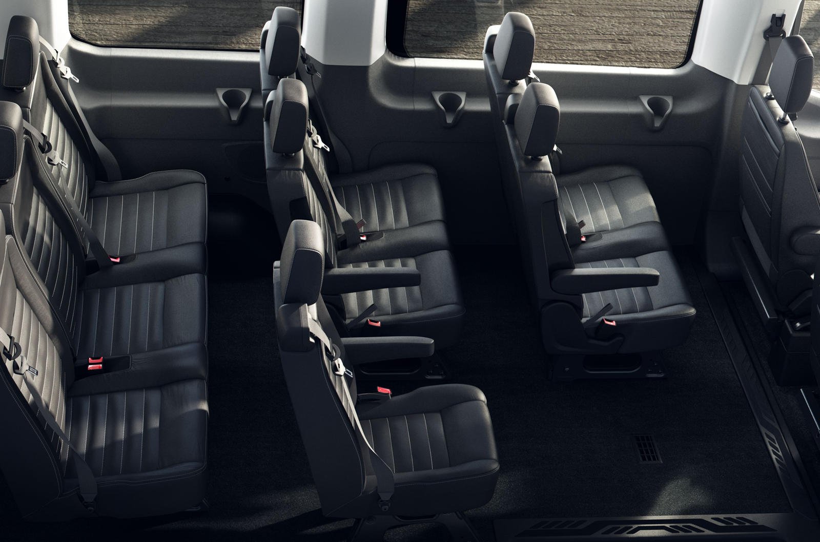 Interior of a passenger van showing two rows of black leather seats with headrests, seat belts, and armrests, and large side and rear windows.