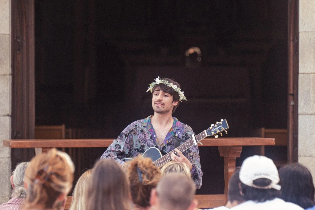 Un homme jouant de la guitare devant un public, portant une couronne de fleurs.