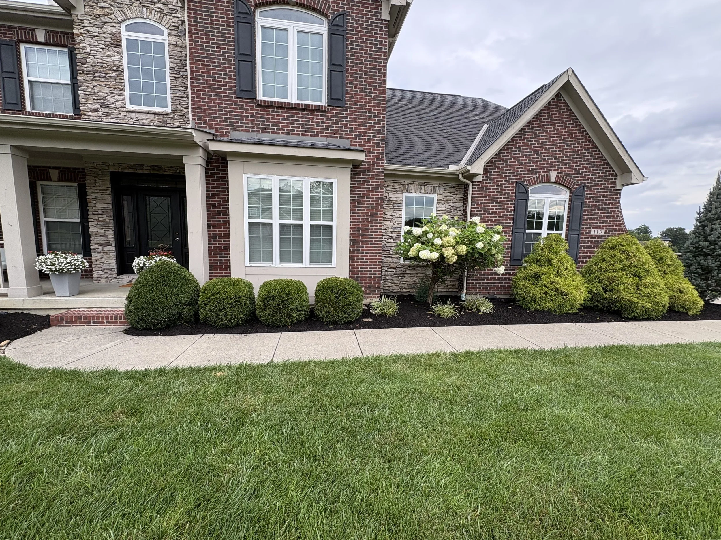 Front view of a brick and stone house with landscaped yard and sidewalk.