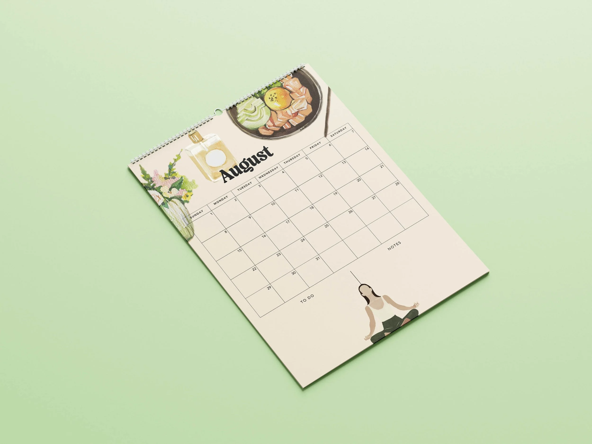 August 2027 page of the Sofe Store wall calendar lying at an angle, with a watercolour poke bowl, a vase of flowers, a perfume bottle, a woman meditating, a Sunday-to-Saturday date grid and To Do list
