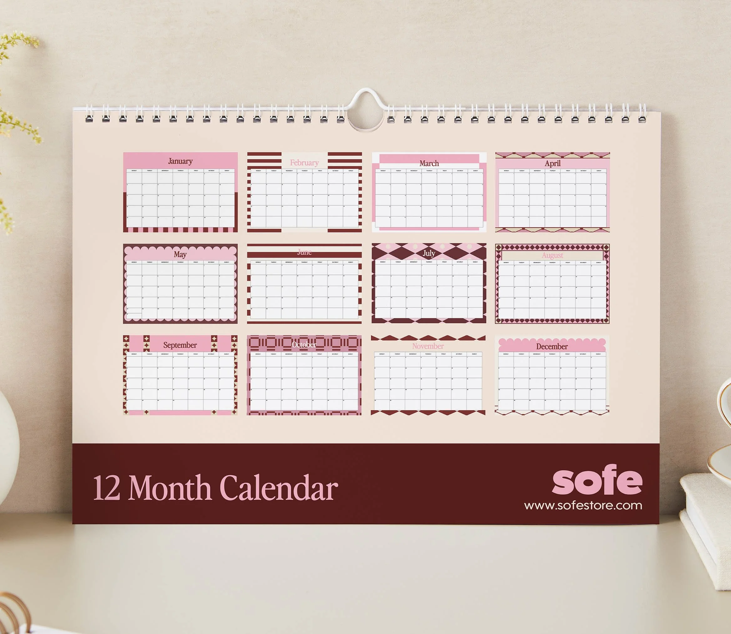 Close-up of the 12 Month Calendar back cover showing twelve pink, burgundy and cream monthly page designs, from scalloped May to harlequin July and checkerboard October