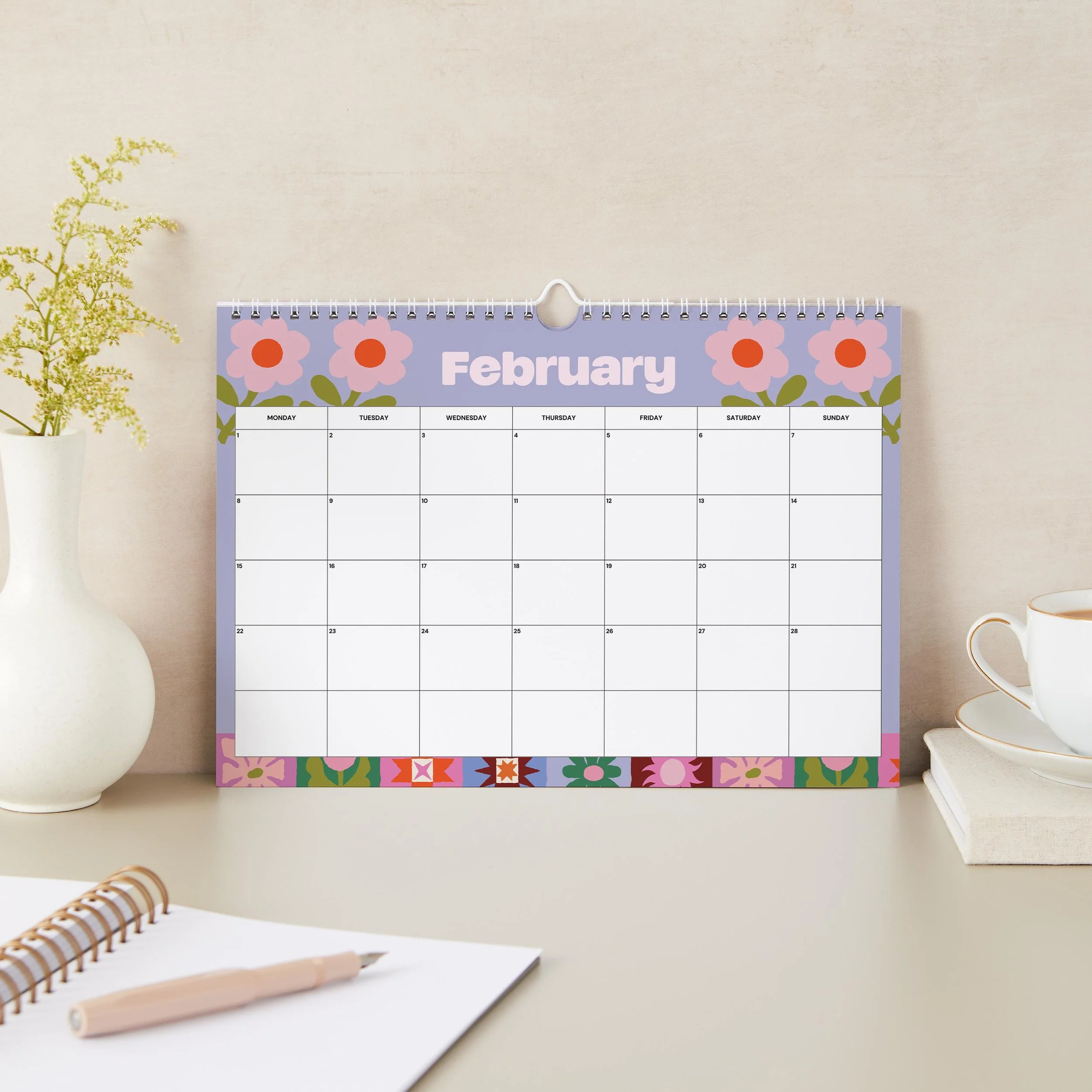 February 2027 page of the Sofe Store wall calendar with a lilac background, pink and orange flowers, and a patchwork flower border along the bottom
