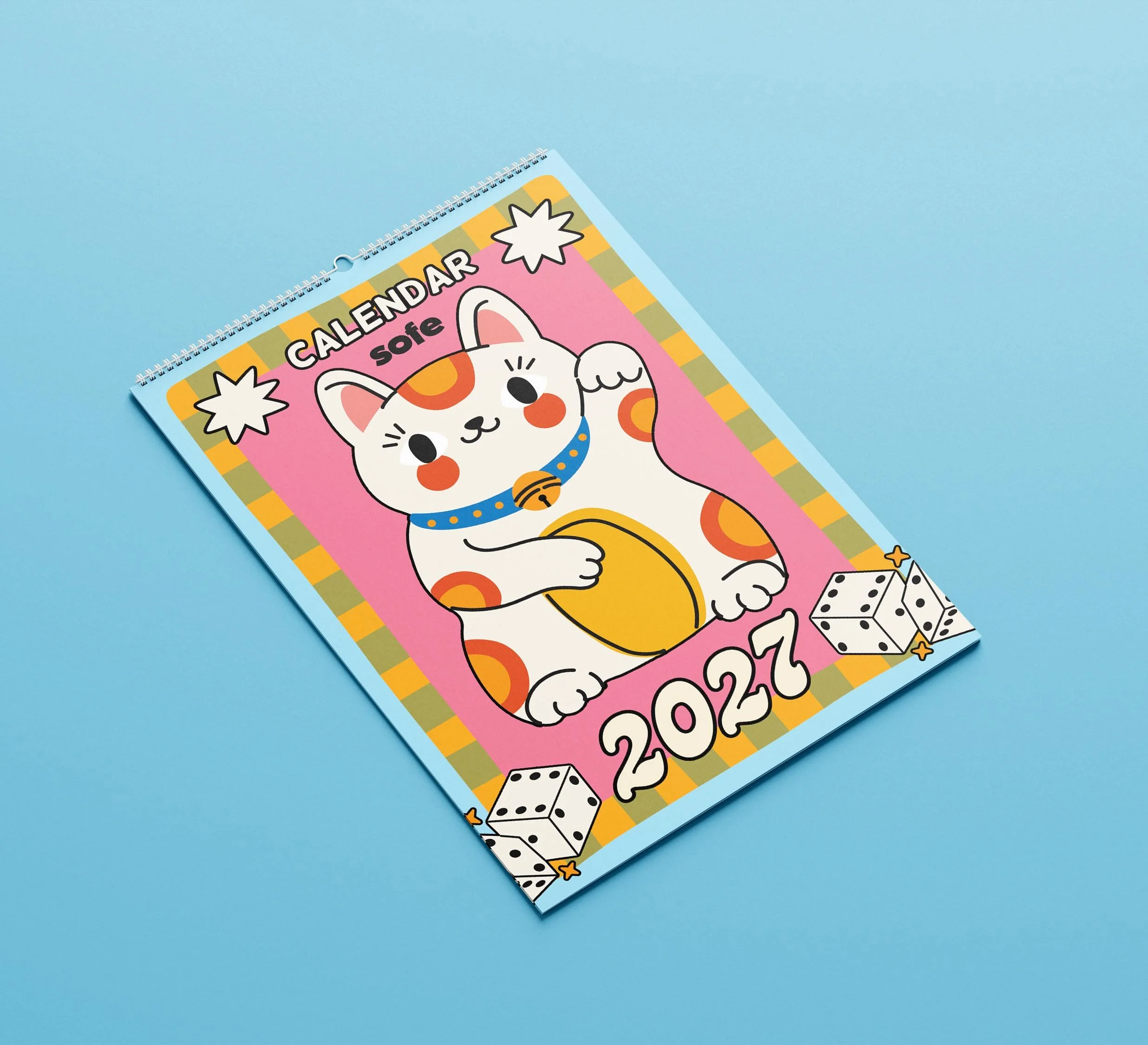 Sofe Store 2027 lucky cat wall calendar lying at an angle on a blue background, showing the maneki-neko cover with dice and star illustrations