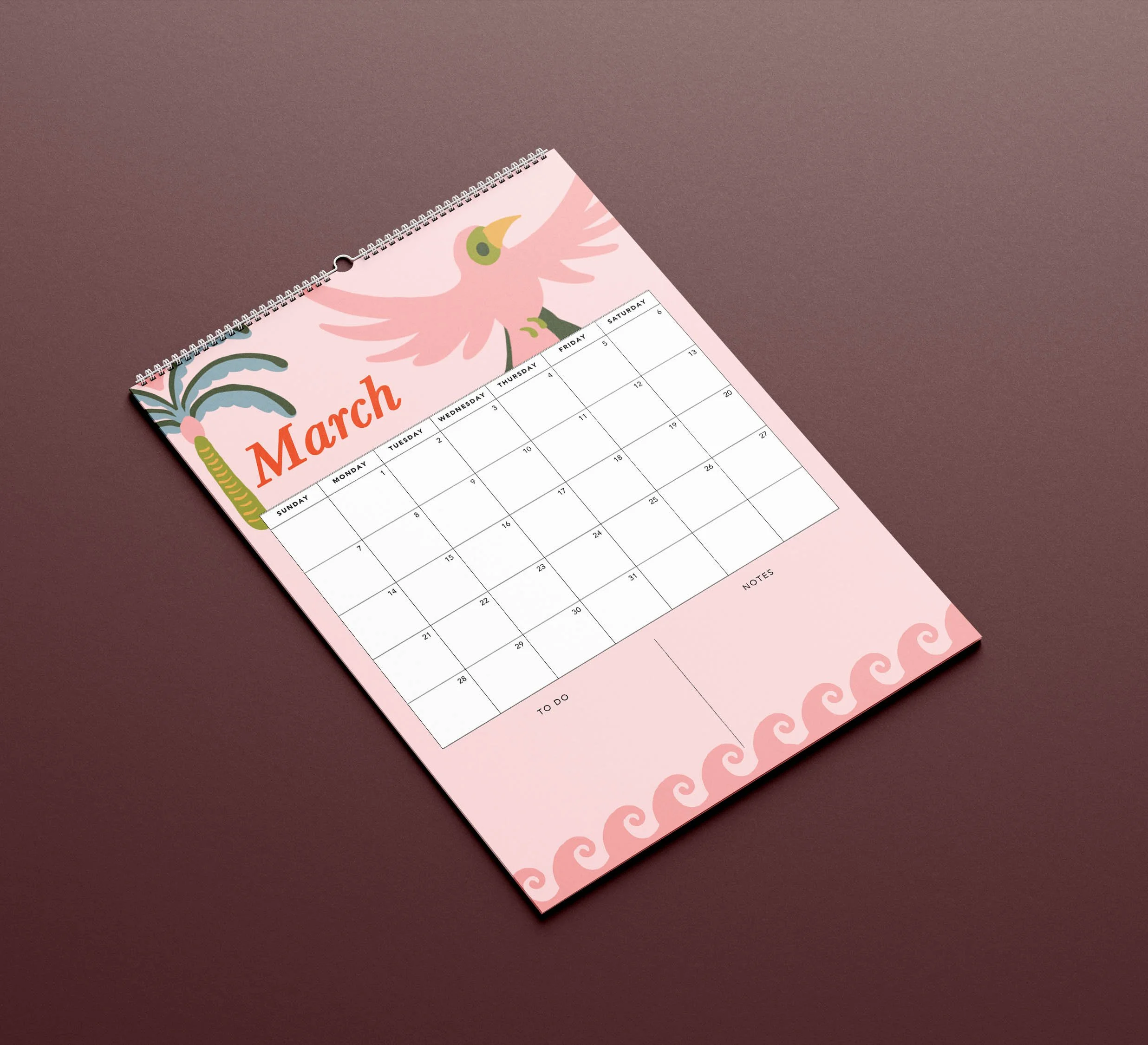 March 2027 page of the Sofe Store wall calendar lying at an angle, with a pink bird, palm tree and wave border above a large date grid