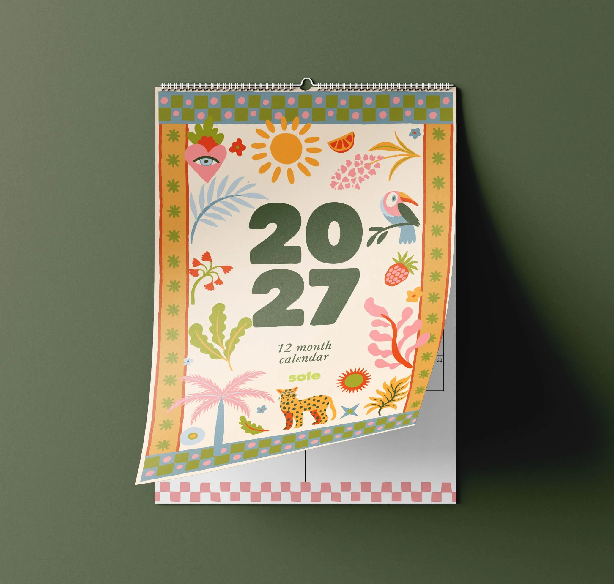 Sofe Store 2027 illustrated wall calendar with the tropical cover page curling up to reveal the monthly planner page beneath, on a green background