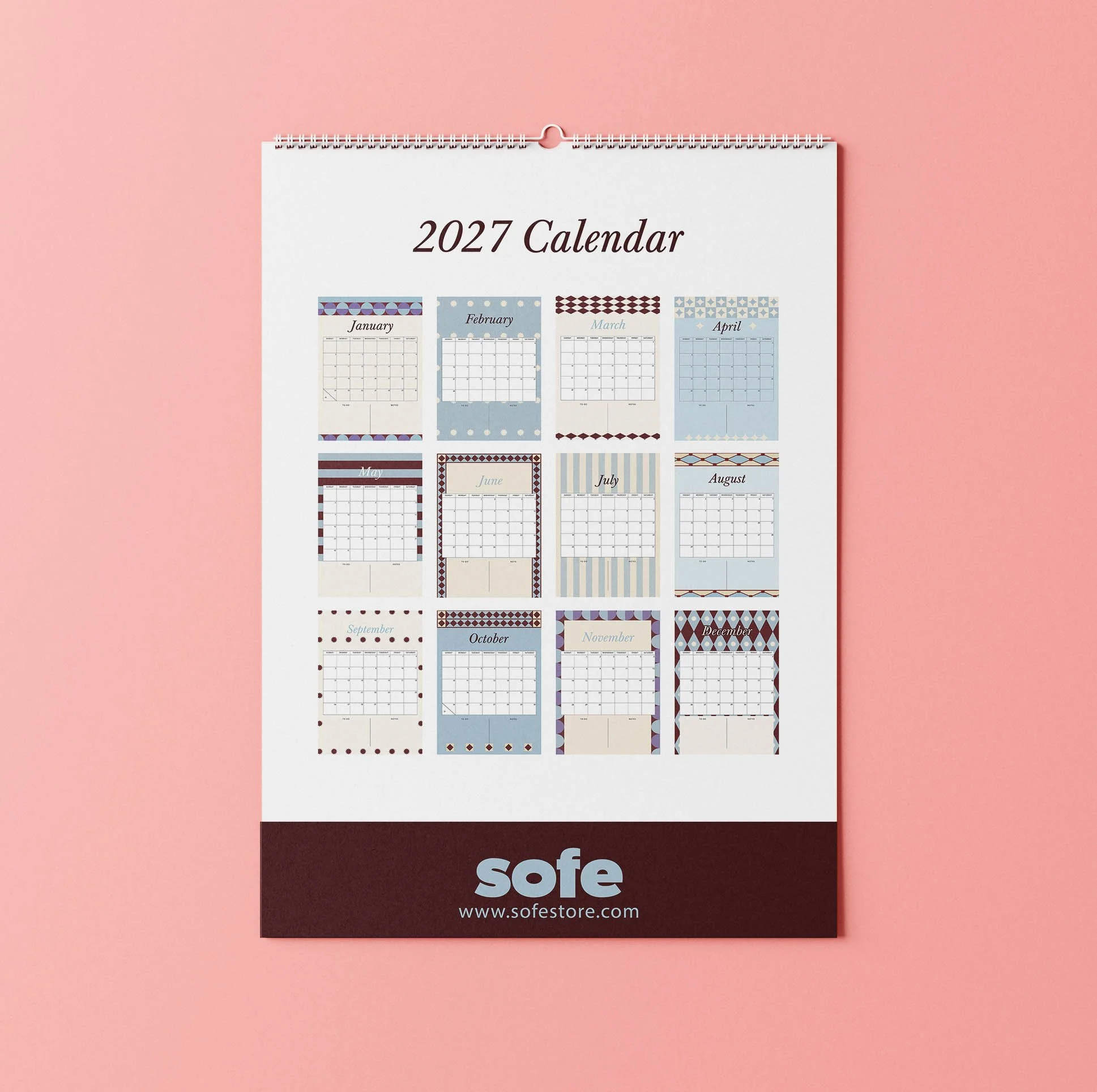 Back page of the Sofe Store 2027 wall calendar showing a mini preview of all twelve months, each with its own burgundy, blue and cream geometric pattern, above a burgundy band with the Sofe Store logo