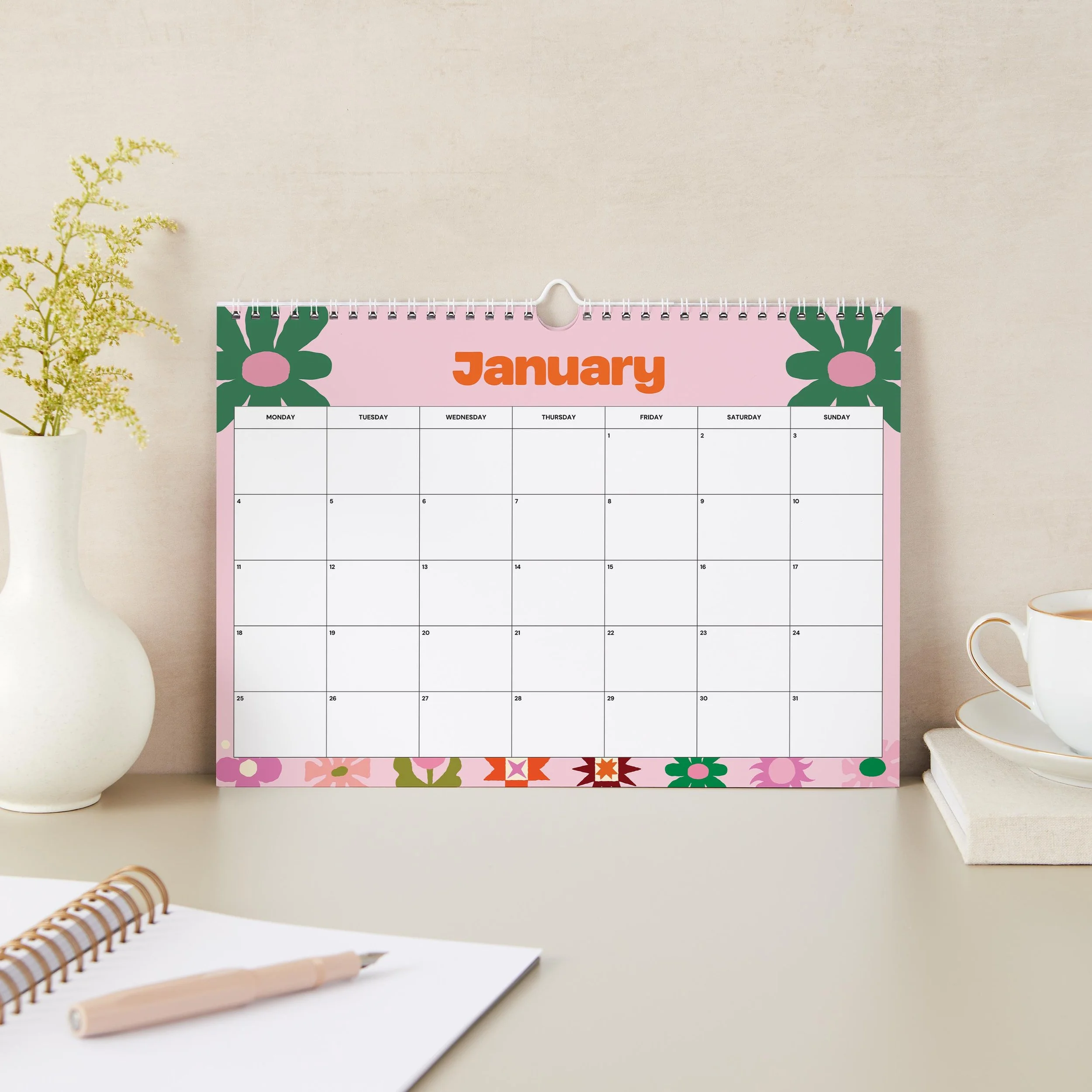 anuary 2027 page of the Sofe Store wall calendar with a pink background, green flowers in the corners, an orange “January” heading and spacious date boxes