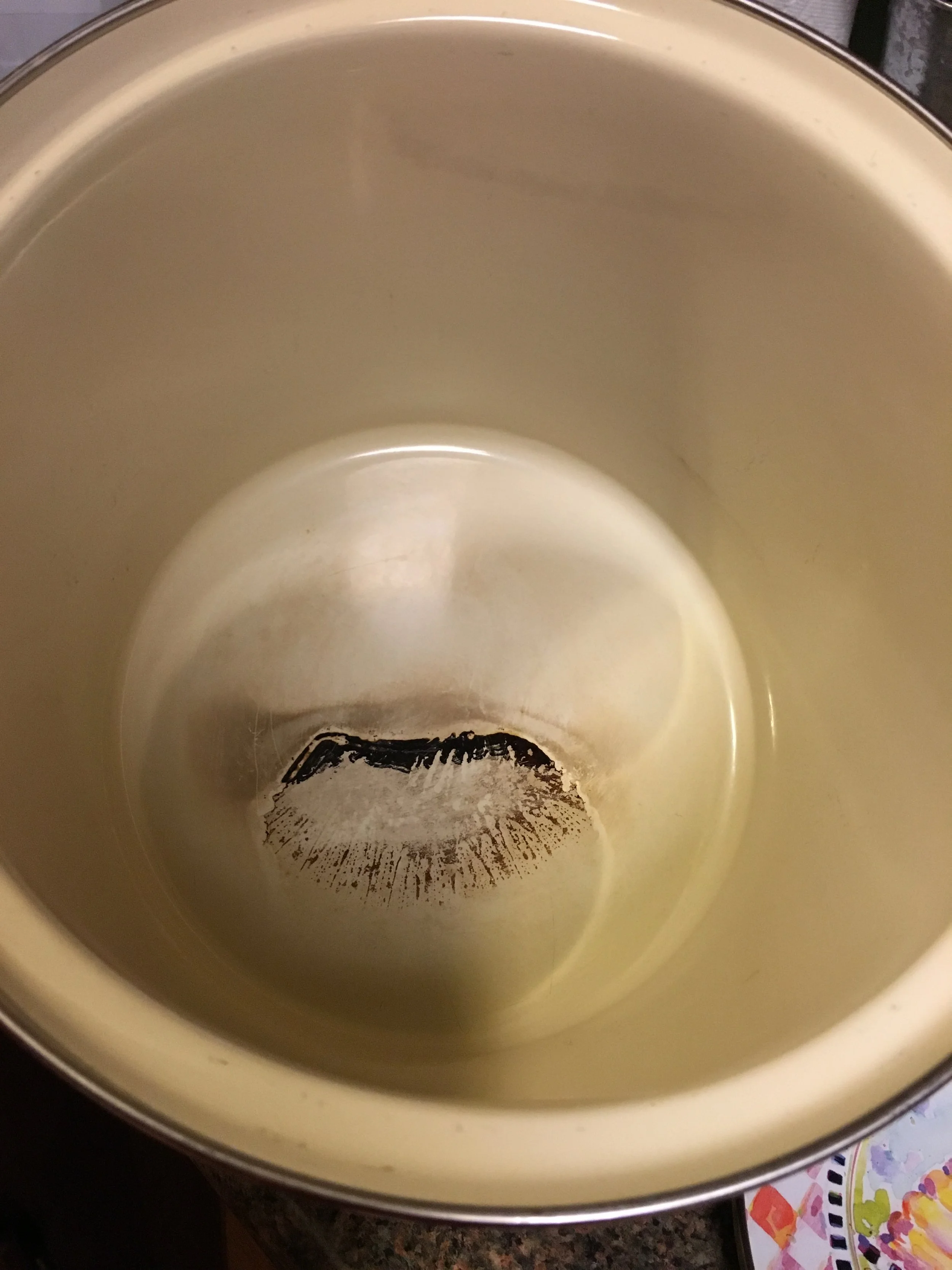 Empty beige mug with black lipstick stain at the bottom, sitting on a dark countertop with colorful patterned paper in the background.