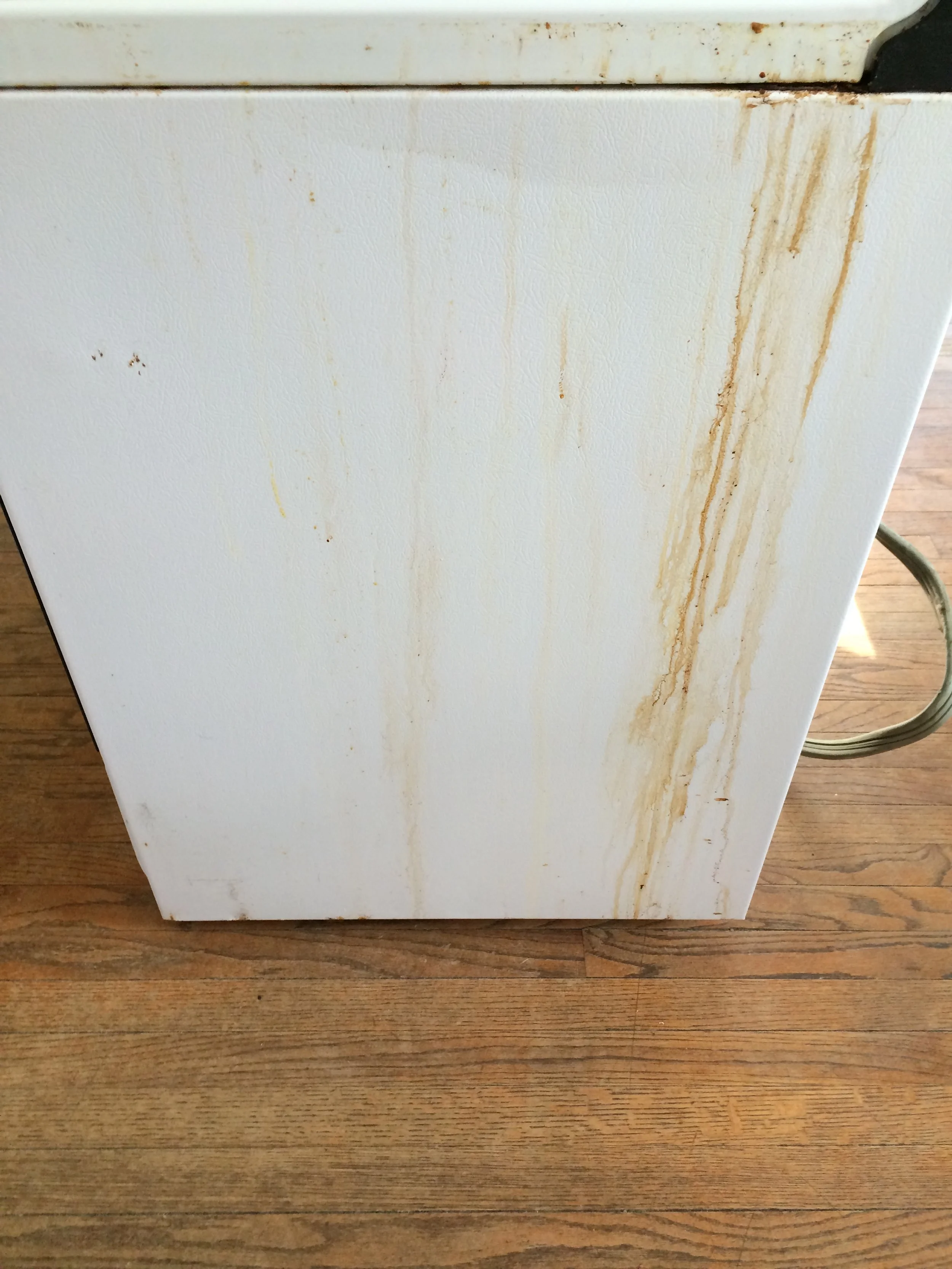 A white appliance with rust stains and areas of discoloration, sitting on a wooden floor.