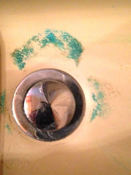 Close-up of a sink drain with blue and green paint smudges on the surrounding surface.