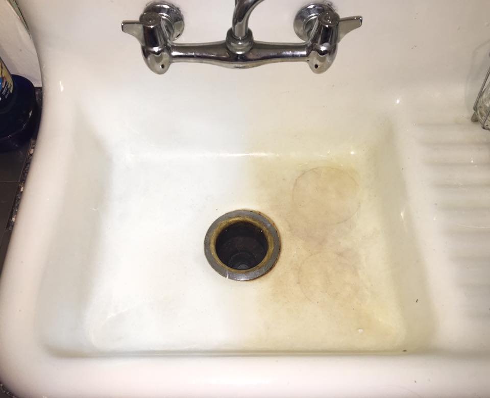 Dirty kitchen sink with a faucet, showing stains and discoloration around the drain.