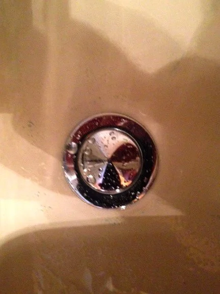 Close-up of bathroom bathtub drain with a shiny silver drain cover.