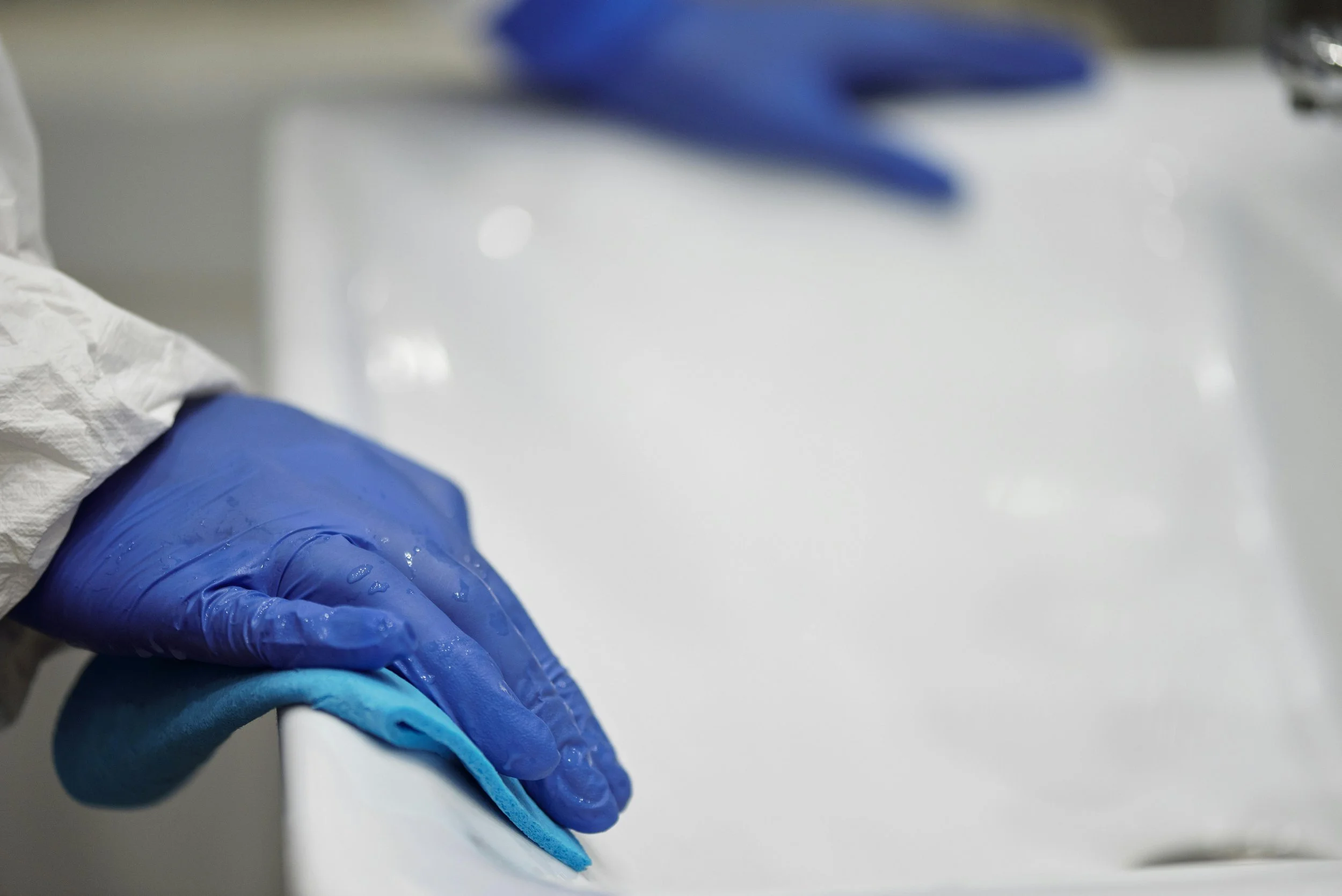 A hand wearing a blue glove holding a white cloth to clean a surface.