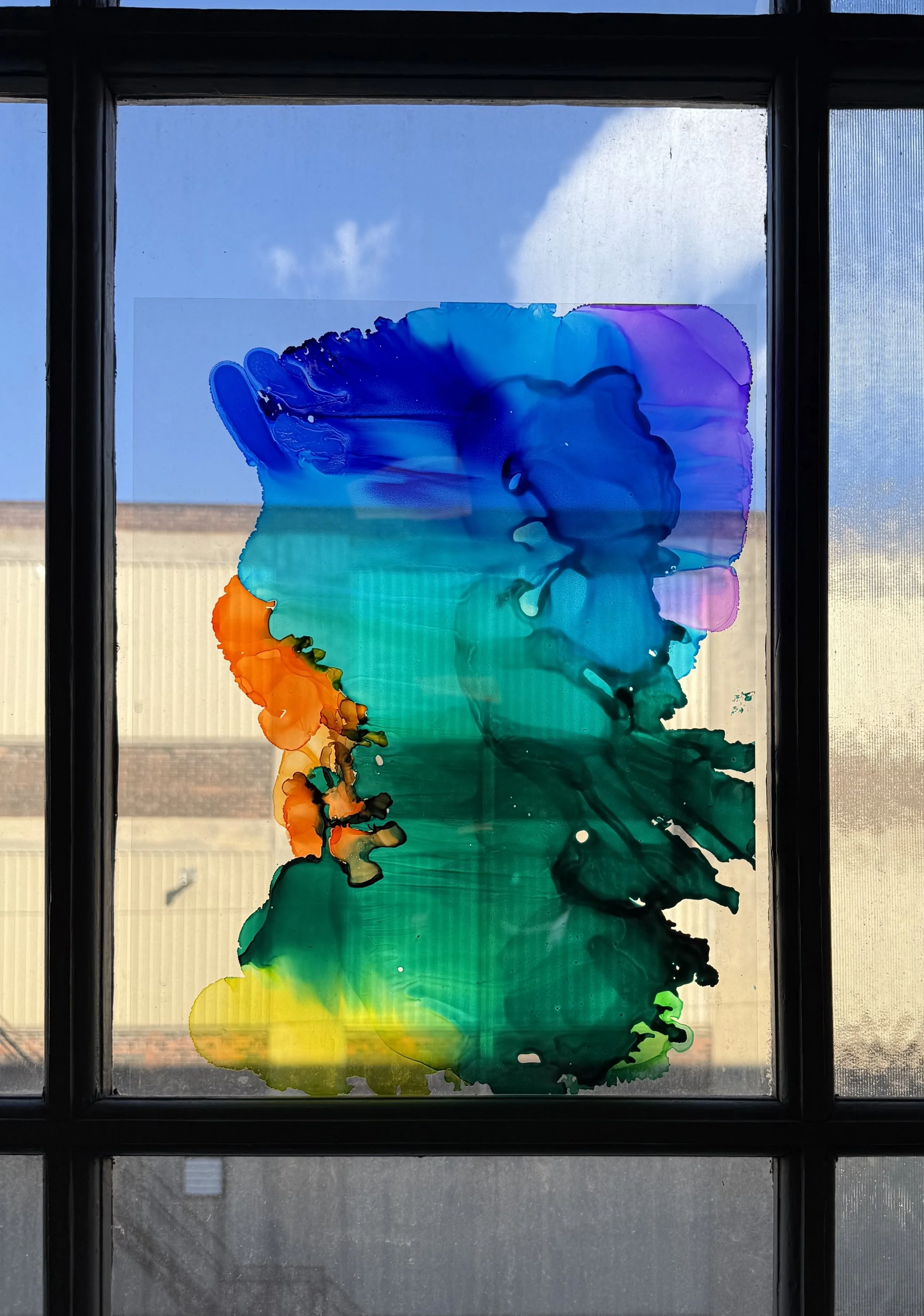 Colourful abstract ink painting on a window in front of a blue sky and a building.