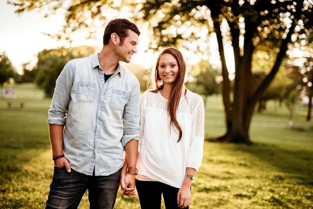 A young couple walking hand-in-hand in a park during sunset, smiling and enjoying each other's company.