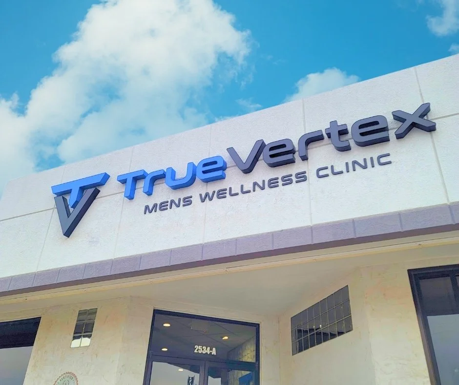 Exterior view of TrueVortex men's wellness clinic sign on building with blue sky and clouds.