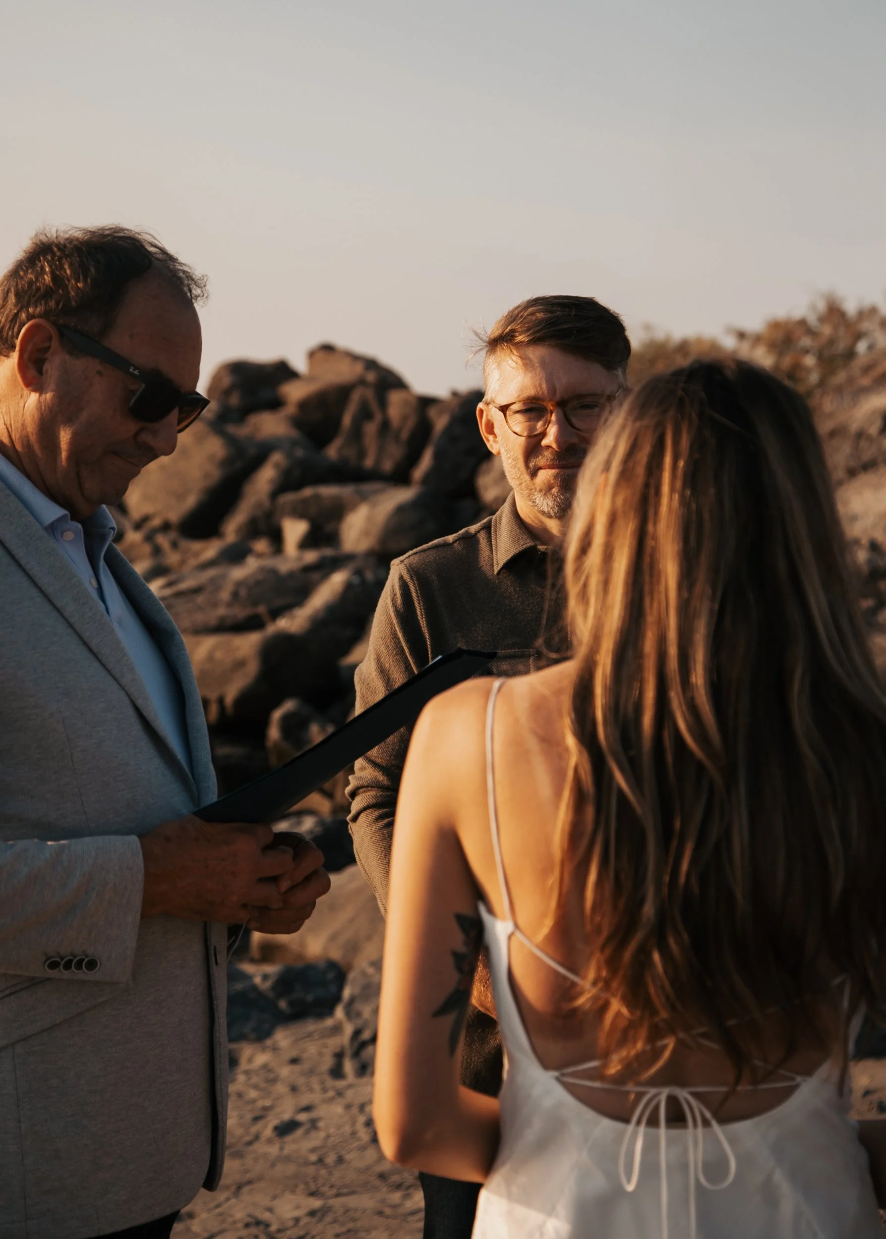A couple getting married on the beach while an officiant conducts the ceremony at sunset. Discovery Park Beach Lighthouse elopement
