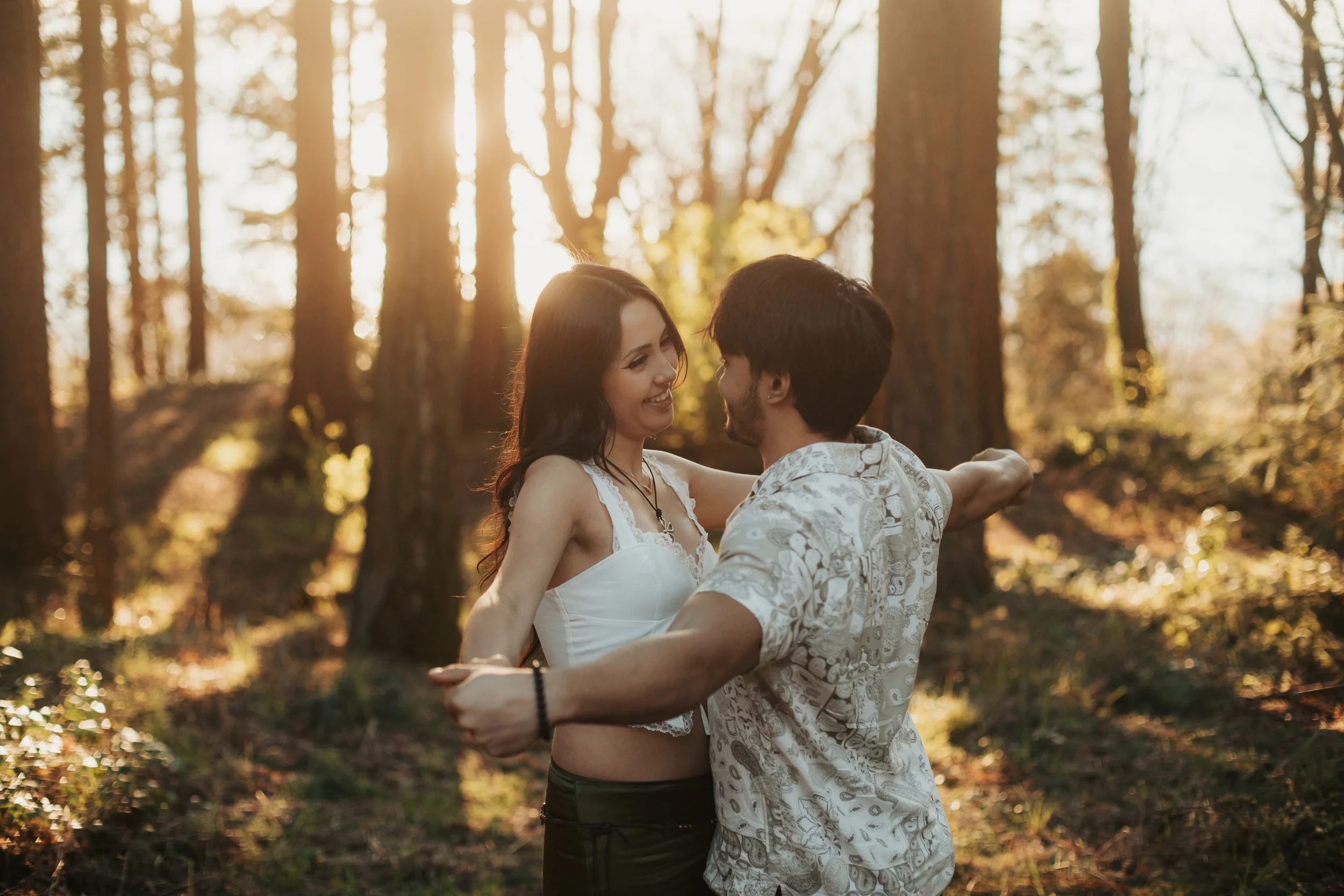 A couple dancing and smiling in a sunny forest during sunset. Golden Gardens park engagement photos
