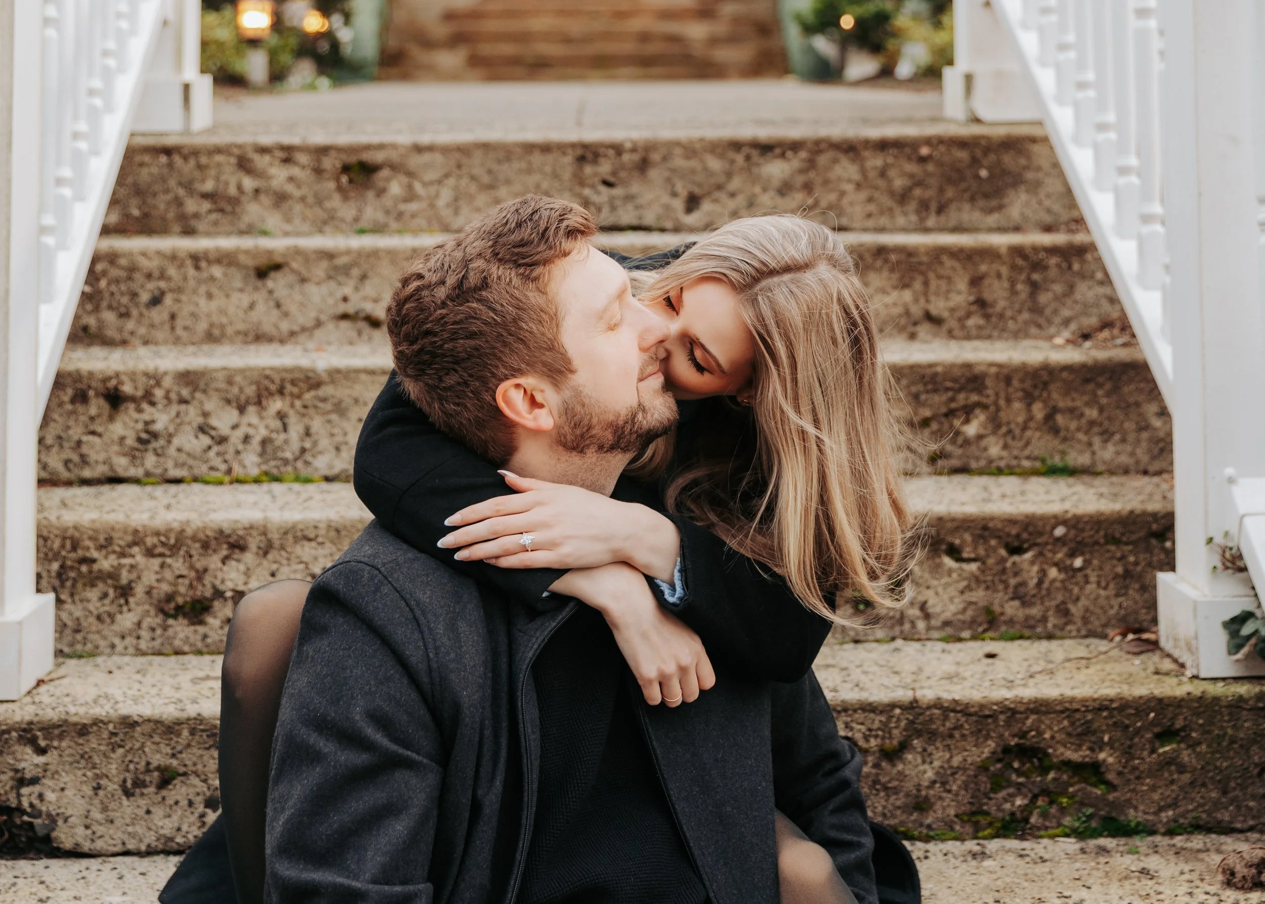 A couple sitting on the ground, embracing and kissing on a set of outdoor stone steps.