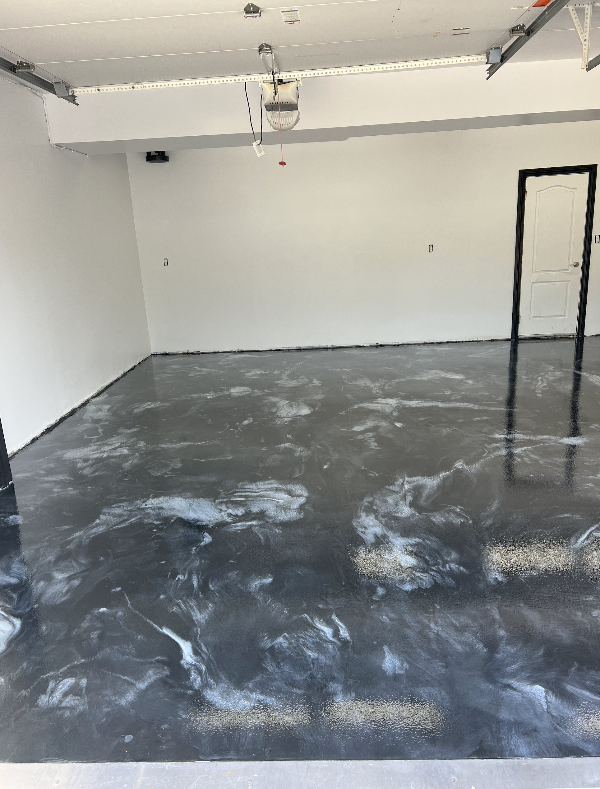 Empty garage with a concrete floor, white walls, a closed door, and a garage door opener mounted on the ceiling.